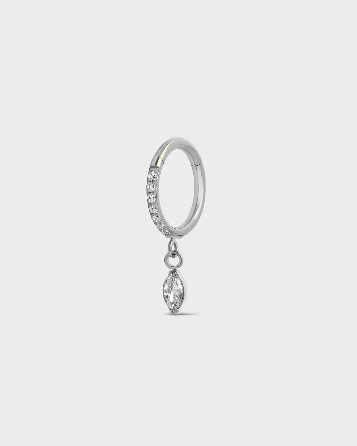 Polished silver titanium hinged ring with clear pave gemstones around the outer edge and a single dangle marquise charm sat on a light gray background.