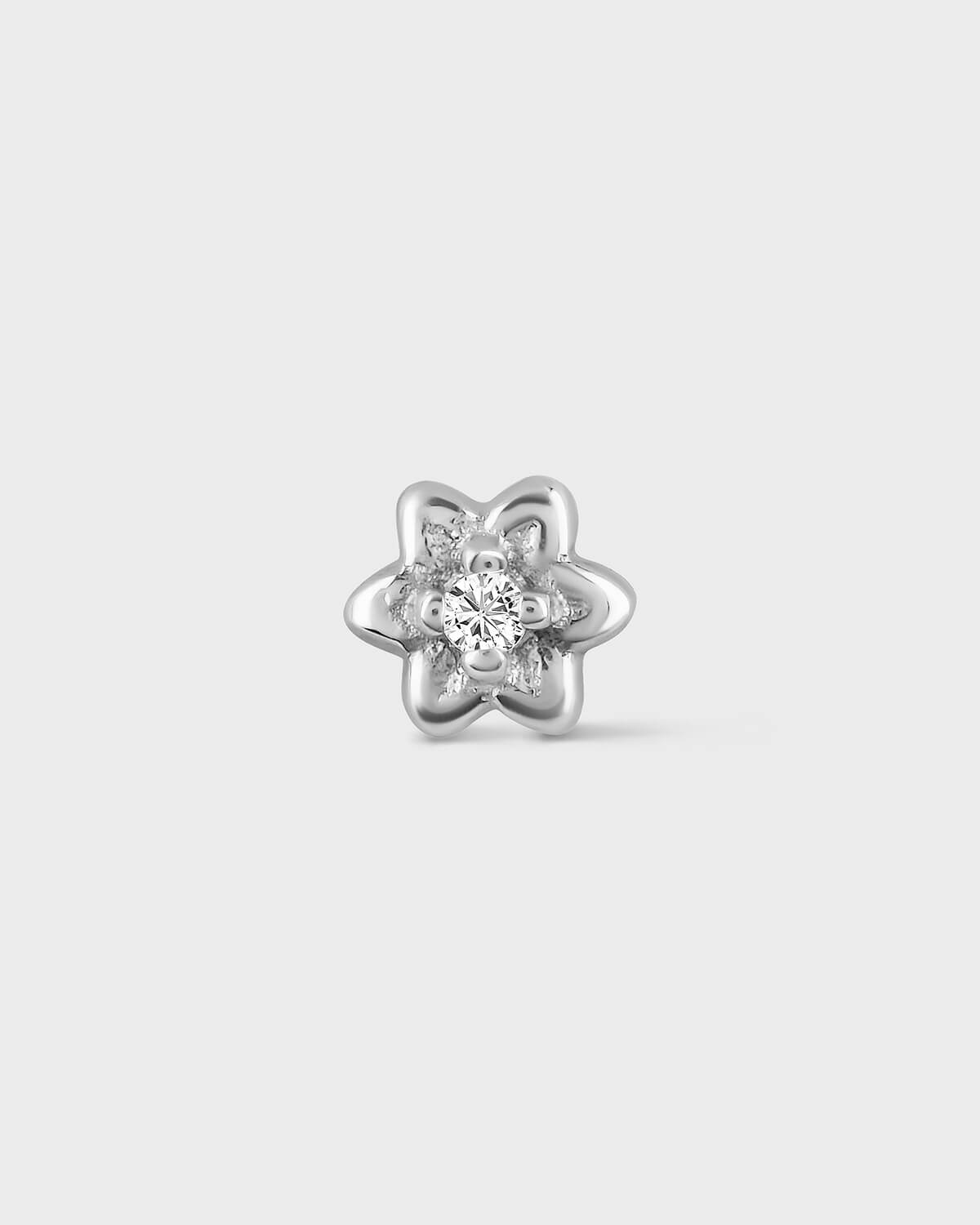 Product photo of a small white gold flower earring with a central clear gemstone sat on a light gray background