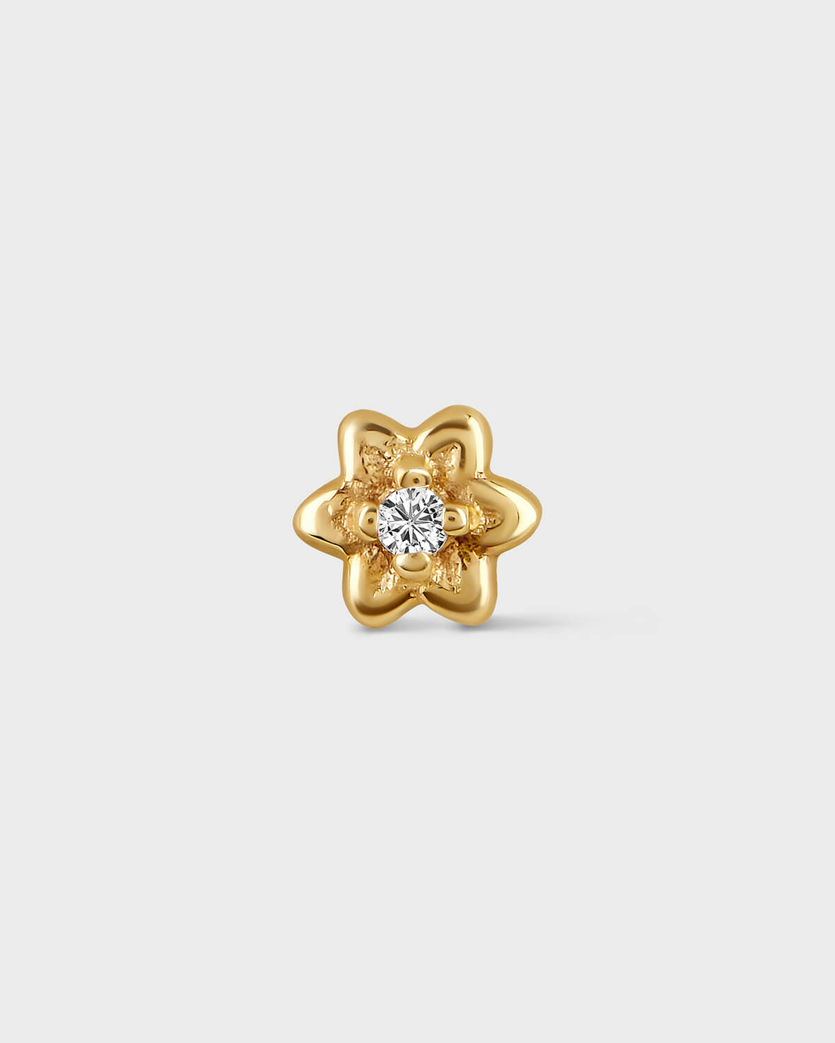Product photo of a small yellow gold flower earring with a central clear gemstone sat on a light gray background