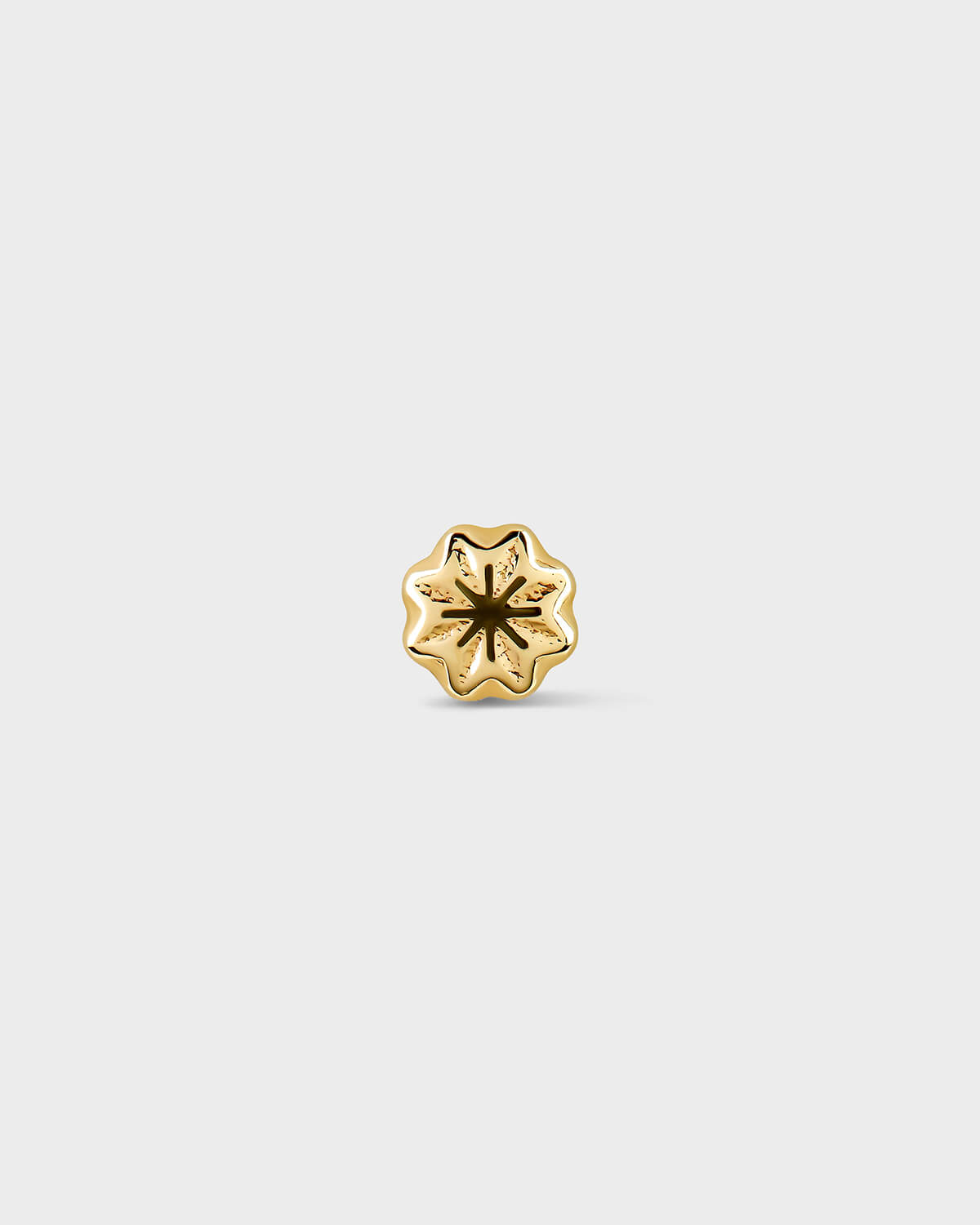 Gold flower-shaped earring on a light gray background